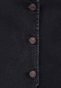 Schwarzer Denim-Stoff mit vier bronzefarbenen Knöpfen. Die Oberfläche ist glatt mit subtilen Schattierungsvariationen und einem klassischen Knopfdesign.