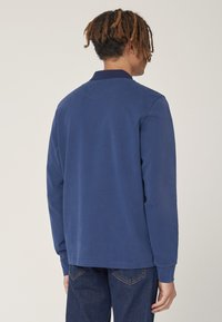 Polo a maniche lunghe navy con colletto piatto, realizzato in cotone morbido, presenta un design semplice e polsini a coste. Indossato con jeans in denim.