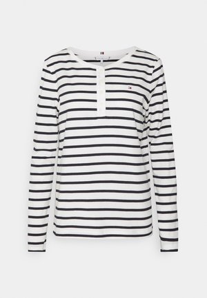 Long-sleeve striped shirt in white and navy, featuring a rounded neckline, button placket, and small logo accent on the chest.