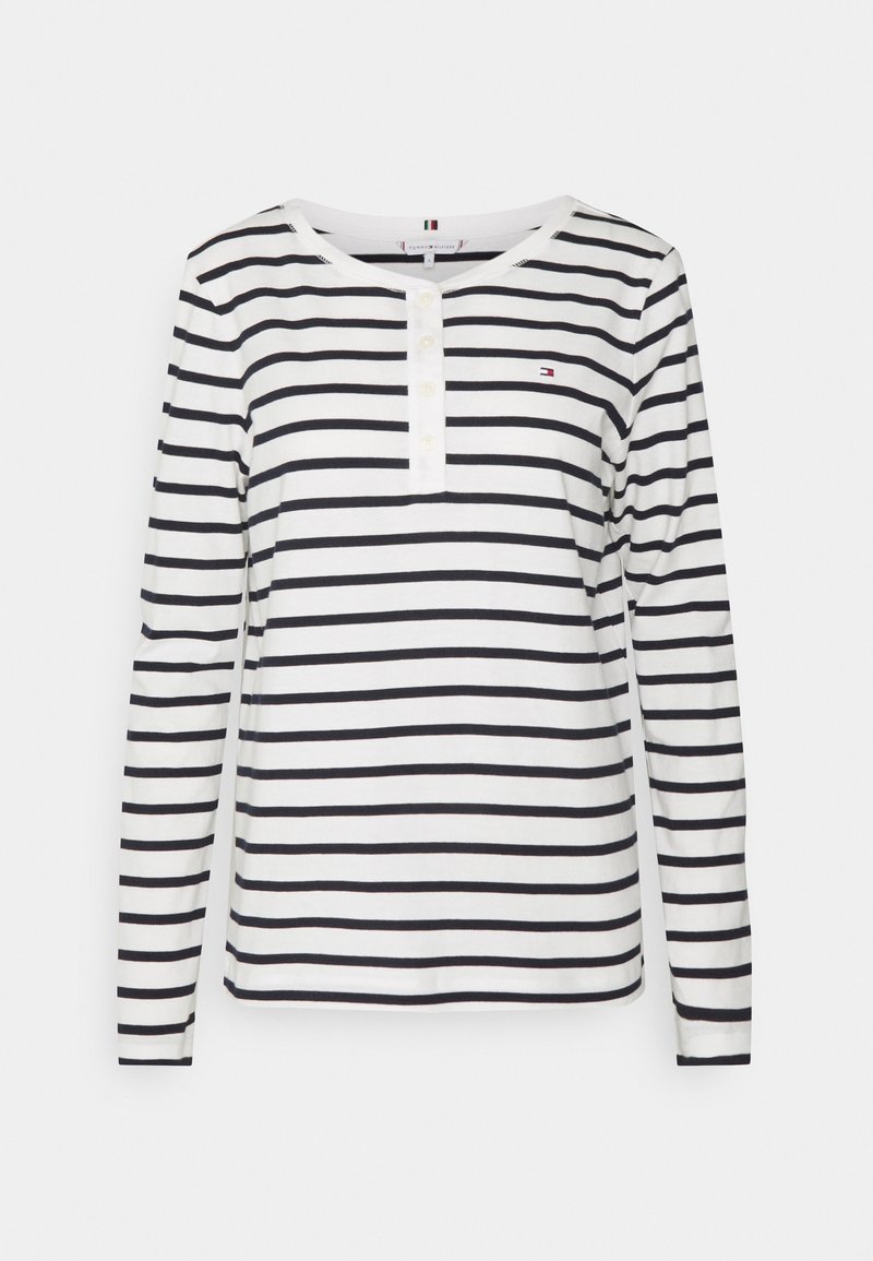 Long-sleeve striped shirt in white and navy, featuring a rounded neckline, button placket, and small logo accent on the chest.