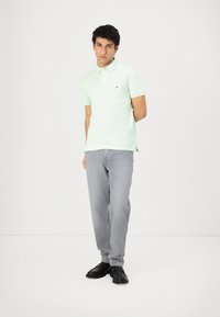 Lys grøn kortærmet polo skjorte med krave, prydet med et lille logo, parret med lys grå jeans og sorte sko.