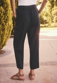 Donkerblauwe broek met een elastische tailleband, taps toelopende pasvorm en twee achterzakken; gecombineerd met lichtbruine sandalen.
