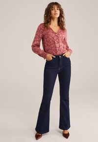 Långärmad blus med v-ringning i dammrosa med ett texturerat mönster; kombinerad med högmidjade, mörkblå utsvängda jeans och bruna klackar.