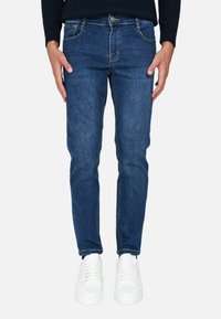 Jeans in denim blu con vestibilità slim, design a cinque tasche, leggera scoloritura e cuciture a contrasto, abbinati a sneakers bianche.