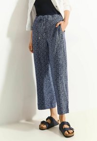 Navy floral print trousers with a relaxed fit, drawstring waist, and side pockets. Paired with dark navy sandals featuring a buckle.