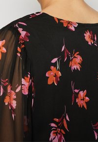 Svart tyg med orange och rosa blommönster, med genomskinliga ärmdetaljer. Mjuk textur och flödande design. Rund halsringning.