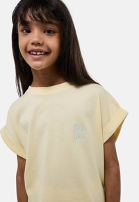 T-shirt en coton jaune avec des manches retroussées, ornée d'un texte brodé bleu clair : "Playa, Siesta, Fiesta." Texture lisse, coupe décontractée.