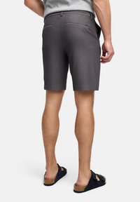 Gråstribede shorts lavet af tekstureret stof, med baglommer og båret med mørke slidesandaler. Tæt fokus på bagvyn.
