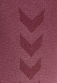 Maroon-kangas, jossa on teksturoitu kuvio, jossa on hieman tummemmasta sävystä koostuvia chevron-muotoja. Sileä pinta, jossa on kevyt kiilto.