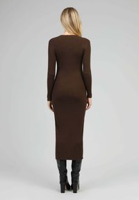 Robe longue à manches longues en maille côtelée marron, silhouette ajustée, atteignant le milieu du mollet, associée à des bottes noires jusqu'aux genoux.