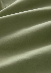 Gros plan d’un tissu vert clair lisse avec des plis doux et une texture fine de tissage diagonal visible.