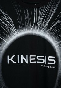 Czarny materiał z białym wzorem przypominającym zaćmienie słońca oraz promieniującymi liniami, z napisem "KINESIS subconscious" na białym tle.