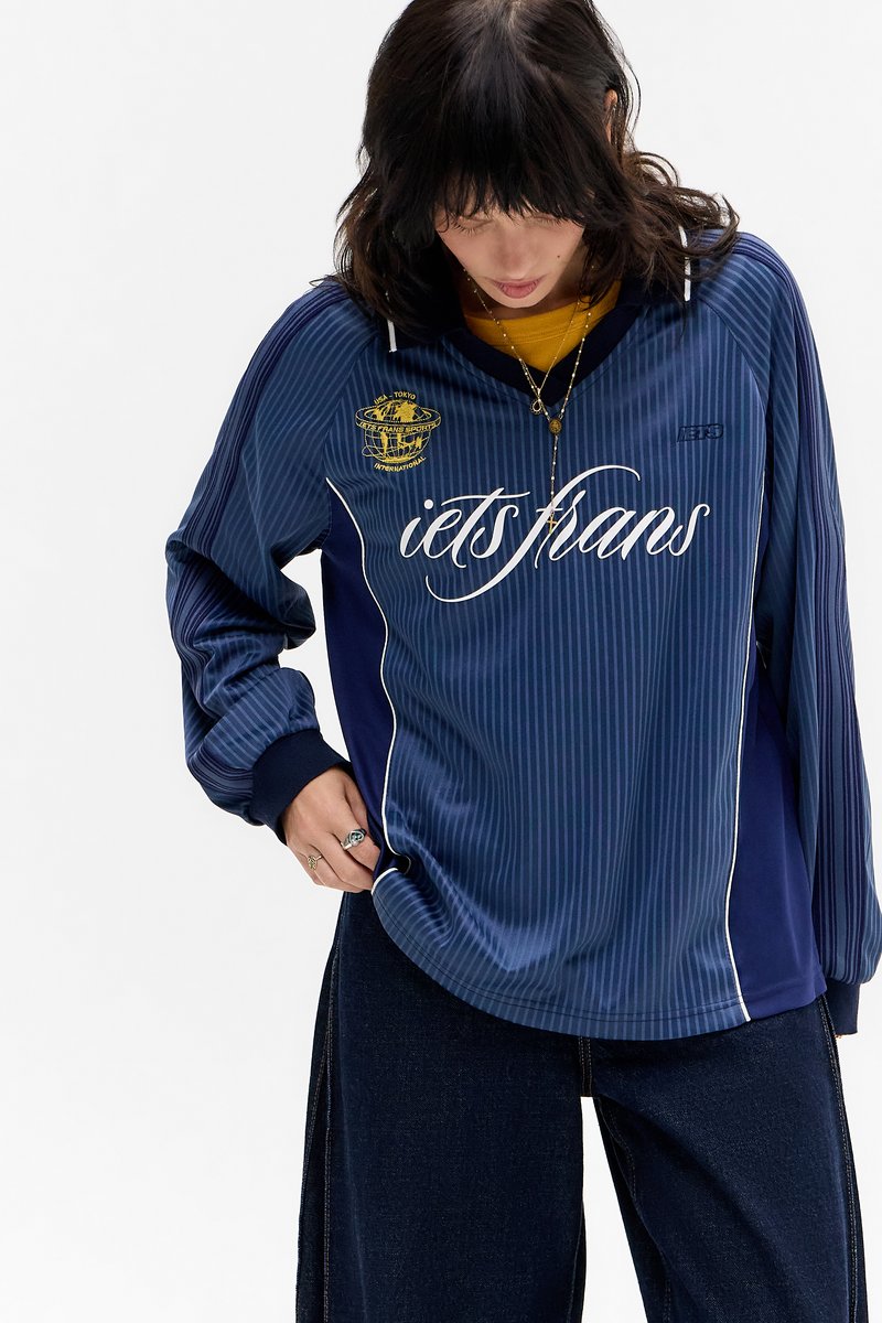 Jersey azul-marinho de manga longa com riscas verticais, punhos canelados, texto branco e um logotipo gráfico amarelo no lado esquerdo do peito, ajuste casual.