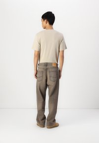 T-shirt beige associé à un jean gris foncé, ample, avec des coutures visibles, des poches arrière et une étiquette en cuir beige sur la ceinture.