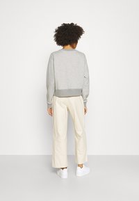 Šedá mikina s žebrovaným lemem a manžetami, kombinovaná s béžovými kalhotami s širokými nohavicemi a bílými teniskami. Hladká textura látky, uvolněný střih.