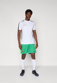 Nike hvid kortærmet skjorte med sorte detaljer, grønne shorts med Barcelona-logo, hvide sokker og sorte fodboldstøvler med blå detaljer.