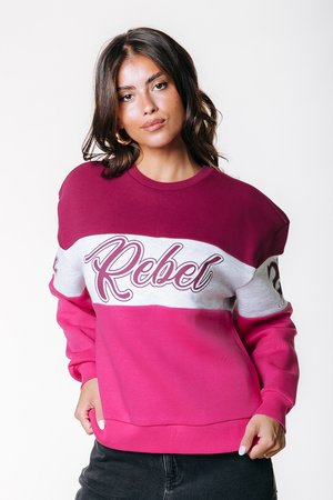 Sudadera en bloque de color rosa y burdeos con "Rebel" impreso en cursiva blanca. Presenta puños acanalados y una textura suave.