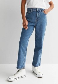 Höga rakben, blå denimjeans med en klassisk femficksdesign, med knappstängning och sömdekorationer. Matchas med vita sneakers.