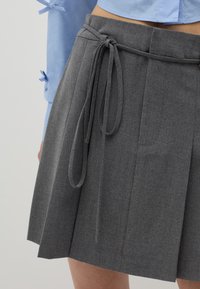 Falda gris con pliegues, hecha de un tejido texturizado, que cuenta con un detalle de cintura atada. El diseño incluye un dobladillo liso y recto.