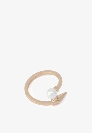 Bague en métal doré présentant une perle blanche lisse et un détail accentué pointu, avec un design simple et ouvert. Nom de la marque gravé à l'intérieur.