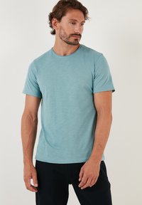 Tricou bleu deschis cu guler rotund, fabricat dintr-un material moale, cu mâneci scurte și o croială lejeră, având o textură subtilă și fără modele vizibile.