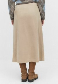 Beige lång kjol i mjukt tyg, med en flödande skärning och lätt lyster, kombinerad med höga bruna stövlar och en mönstrad tröja.