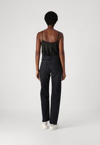 Jeans de mezclilla negra con corte recto y cintura alta, combinados con una blusa sin mangas negra y zapatillas blancas. Textura suave, detalles mínimos.