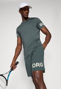 Dark gray athletic t-shirt with "BORG" logo on sleeve, paired with matching shorts featuring larger logo. Player holds a tennis racket.