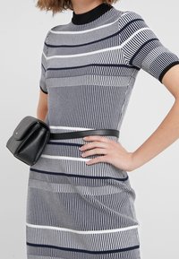 Abito lavorato a maglia con righe verticali blu navy e bianche, maniche corte e collo alto. Abbinato a una cintura con marsupio nero indossata in vita.