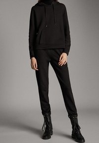 Musta huppari naruilla ja etutaskulla, yhdistettynä mustiin jeepareihin. Raskaat mustat nauhakengät täydentävät asukokonaisuutta.