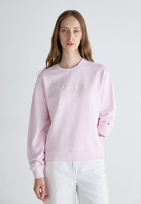 Pink sweatshirt with ribbed cuffs and hem, featuring a subtle embroidered logo on the chest. Made of soft fleece-like material.