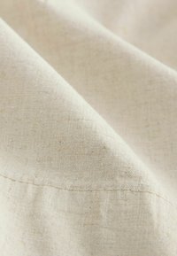 Zbliżenie na beżową tkaninę lnianą z widoczną fakturą splotu i subtelnymi szwami.