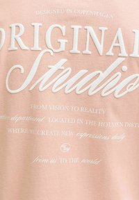 Κείμενο σε ροζ ύφασμα γράφει «Original Studios» με μεγάλα λευκά γράμματα και μικρότερες φράσεις για το σχεδιασμό και τη δημιουργικότητα από κάτω.