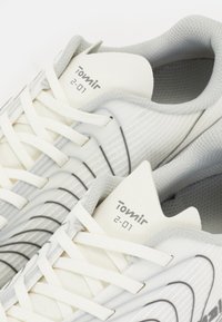 Weiße Sneakers mit einer strukturierten Oberseite, die graue Akzente, dünne schwarze Linien und elastische Schnürsenkel aufweisen. Der Markenname "Tomir" ist auf der Zunge aufgedruckt.