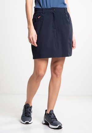 Falda ligera de color azul marino con cintura elástica, bolsillos frontales y detalles cosidos. Llevada con zapatos deportivos oscuros.