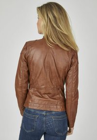Bruine leren jas met een getailleerd ontwerp, zichtbare stiksels en schouderdetails. G gedragen met blauwe denim jeans. Gladde textuur.