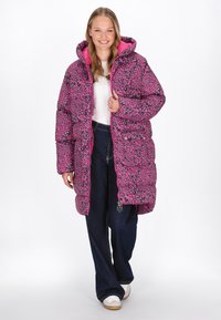 Pufferjakke i lys pink med sort og grøn leopardprint, med hætte og lynlås, suppleret med denimbukser og sneakers.