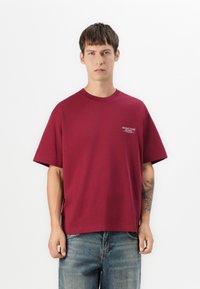Mørkerød bomulds-T-shirt med rund halsudskæring, korte ærmer og en løs pasform. Har et lille trykt logo på venstre bryst.
