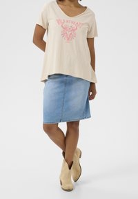 Béžové tričko s krátkým rukávem a V-výstřihem, s růžovým grafickým potiskem, doplněné světle modrou džínovou sukní a béžovými kotníkovými botami. Hladká látka, volný střih.