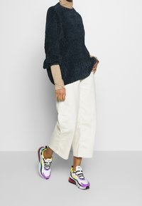 Gruby granatowy sweter w prążki, beżowy golf, kremowe spodnie o szerokich nogawkach oraz kolorowe sneakersy z fioletowymi, żółtymi i turkusowymi akcentami.