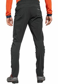 Schwarze Outdoor-Hosen mit einer taillierten Passform, die über Reißverschlusstaschen und vorgeformte Knie verfügen, getragen mit grauen Wanderschuhen.