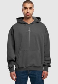 Sudadera de felpa gris con un gran bolsillo frontal, capucha con cordones y texto blanco "PIENSO DIFERENTE" impreso verticalmente en el pecho.