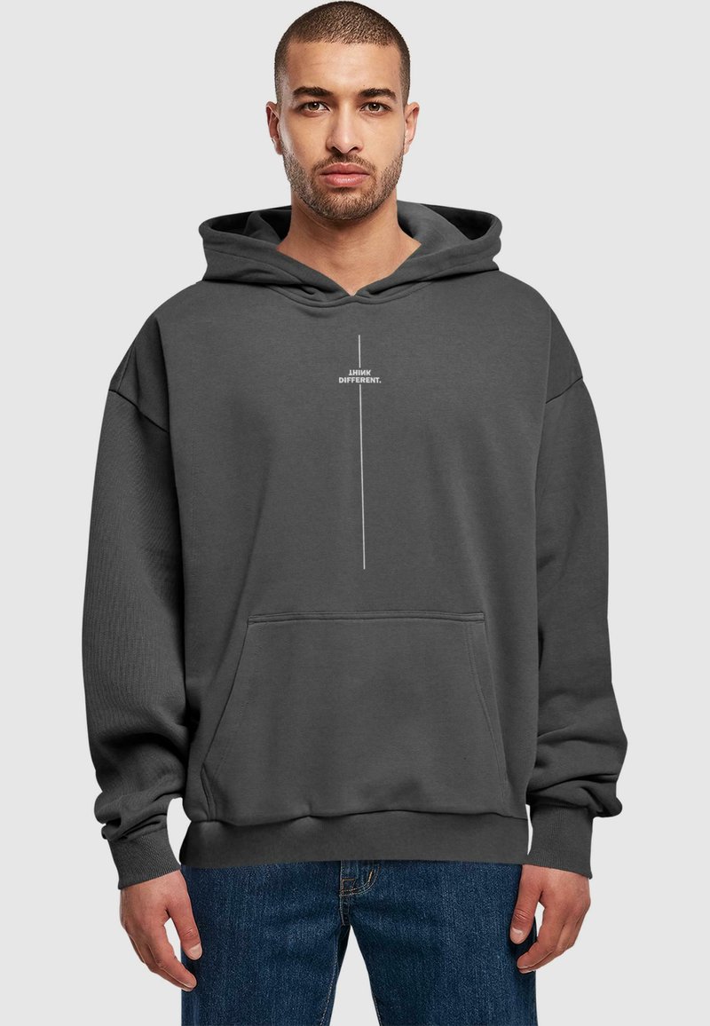 Sudadera de felpa gris con un gran bolsillo frontal, capucha con cordones y texto blanco "PIENSO DIFERENTE" impreso verticalmente en el pecho.