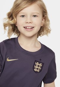 Maglia Nike viola con tessuto testurizzato, scollatura rotonda e logo dorato. Presenta un badge ricamato con leoni e una stella sopra di esso.