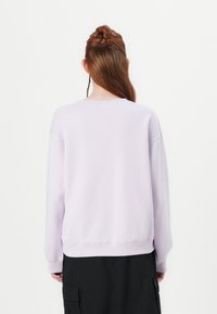 Lichtpaarse trui met geribde hals en manchetten, met een losse pasvorm en licht gestructureerde stof. Draagt zwart cargobroek.