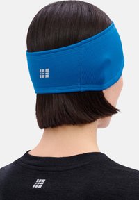 Blauwe stoffen hoofdband met een gestructureerd oppervlak, verstelbare pasvorm en logodetail aan de achterkant. Gecombineerd met een zwart shirt bij de halslijn.