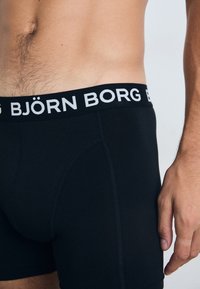 Crne bokserice s debelim crnim elastikom na struku na kojem piše "BJÖRN BORG" u bijelim slovima. Glatka tekstura, prilagođen dizajn.