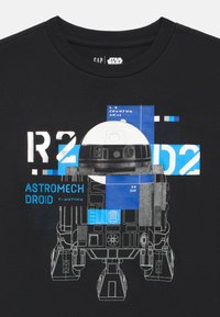 Czarny bawełniany t-shirt z grafiką astromech droida R2-D2 w białym i niebieskim kolorze, z geometrycznymi kształtami i tekstowymi akcentami.