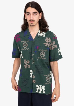 Camicia a maniche corte verde con colletto realizzata in tessuto con motivi floreali e geometrici in viola, bianco e beige. Presenta una tasca sul petto.