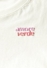 T-shirt en coton blanc avec une texture côtelée et un col rond. Broderie "amore" en rose et "verde" en corail.